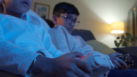 Nahaufnahme-Der-Hände-Von-Zwei-Kleinen-Jungen,-Die-Zu-Hause-Mit-Einer-Computerspielkonsole-Auf-Dem-Fernseher-Spielen-Und-Spät-In-Der-Nacht-Controller-Halten-4